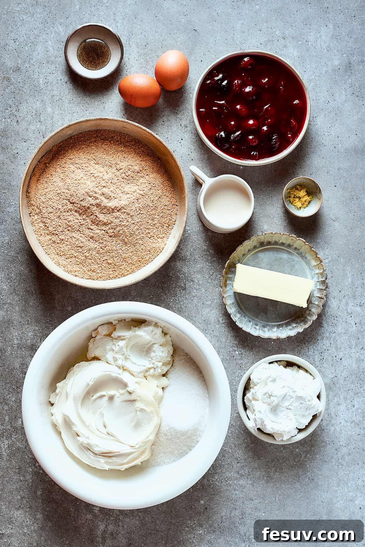 All the fresh ingredients for making cherry cheesecake are neatly arranged on a rustic wooden surface.