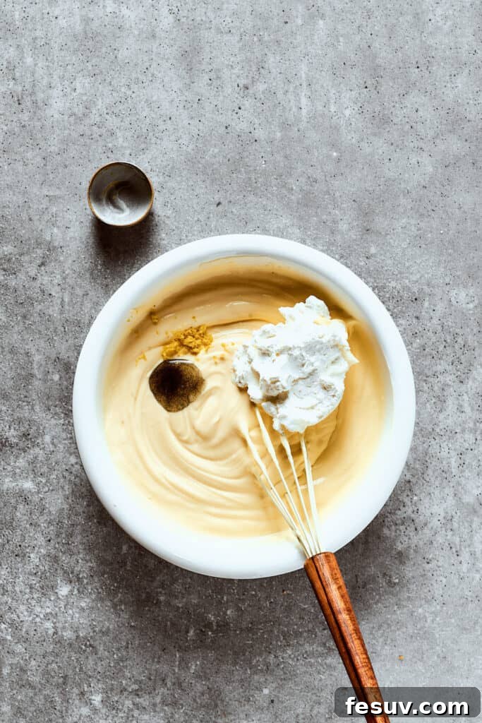 Beating additional ingredients into a large mixing bowl for the cheesecake filling, ensuring a smooth texture.