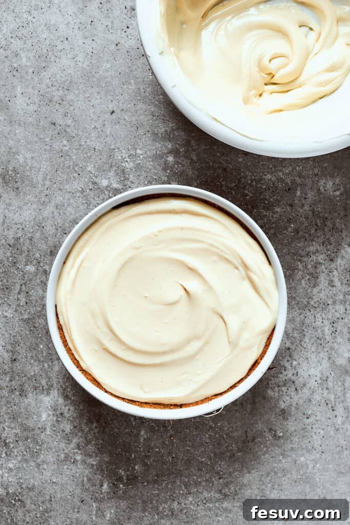 Spreading creamy cheesecake filling evenly into a prepared graham cracker crust in a springform pan.