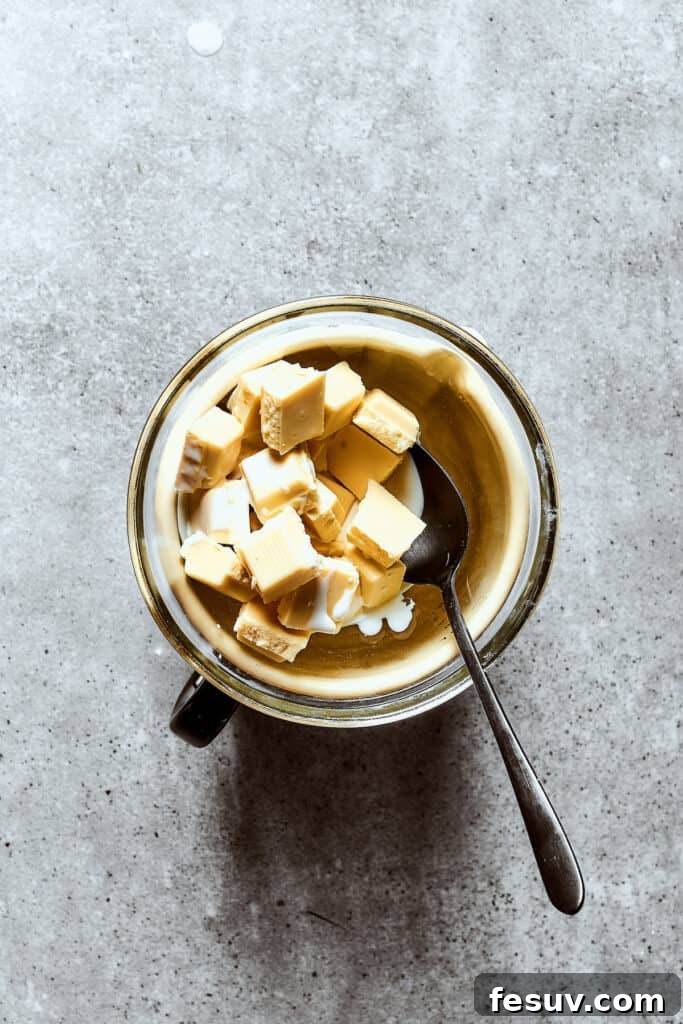 Melting white chocolate chunks with heavy cream in a bowl to create the luscious ganache topping.
