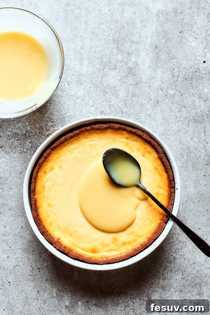 Spreading a smooth layer of white chocolate ganache over the chilled cheesecake, preparing for the cherry topping.