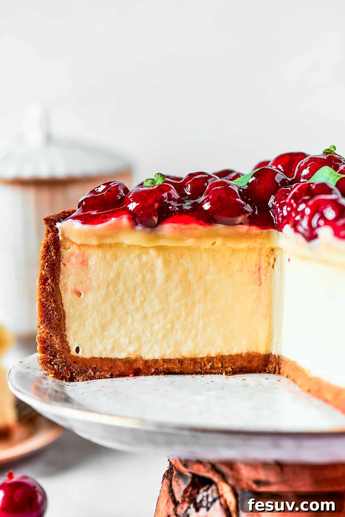 A close-up view of a whole cherry cheesecake, richly topped with cherries and placed on a elegant cake stand, awaiting indulgence.