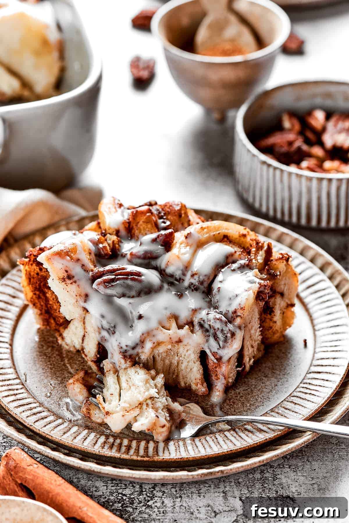 Ooey-Gooey Cinnamon Bake 2 A perfectly baked square of cinnamon roll casserole resting on a white plate, adorned with a swirl of icing, with a fork gently taking a bite. The casserole exhibits a beautiful golden-brown crust and soft, inviting interior.