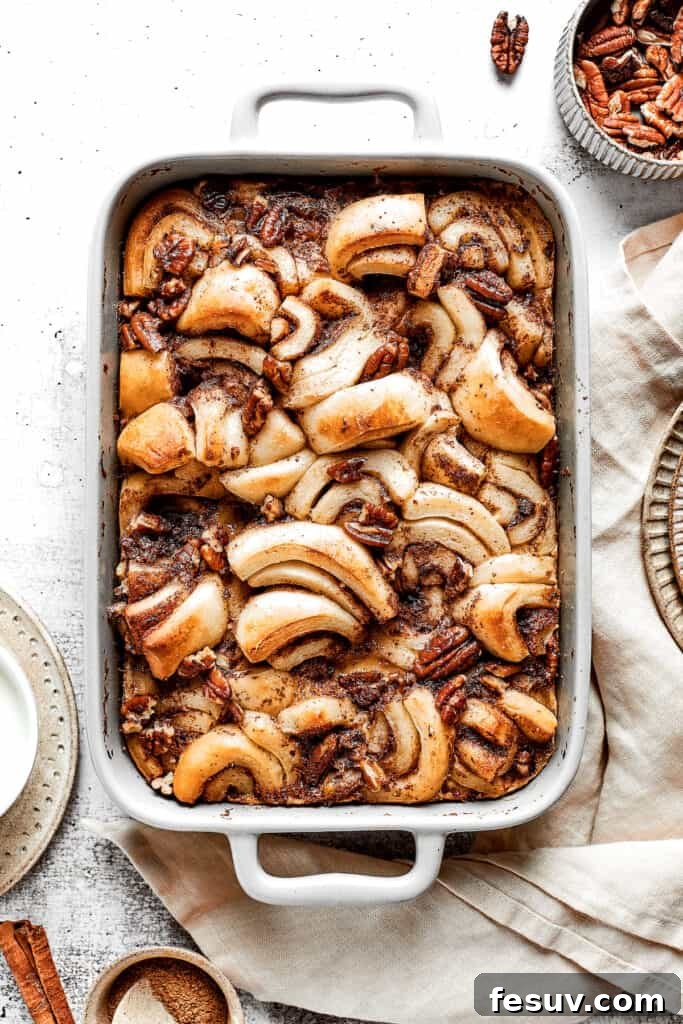 These easy and celebratory cinnamon roll casseroles are rich, creamy, and buttery, and packed with sticky and sweet maple syrup and pecans. A delightful overhead view of a cinnamon roll casserole, freshly baked and golden brown, emerging from the oven. The rolls are puffed and caramelized, promising a soft and delicious treat.