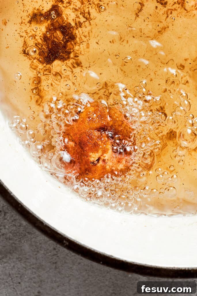 A close-up shot of a single mac and cheese bite sizzling and frying in hot oil within a deep skillet, achieving a perfect golden crisp.