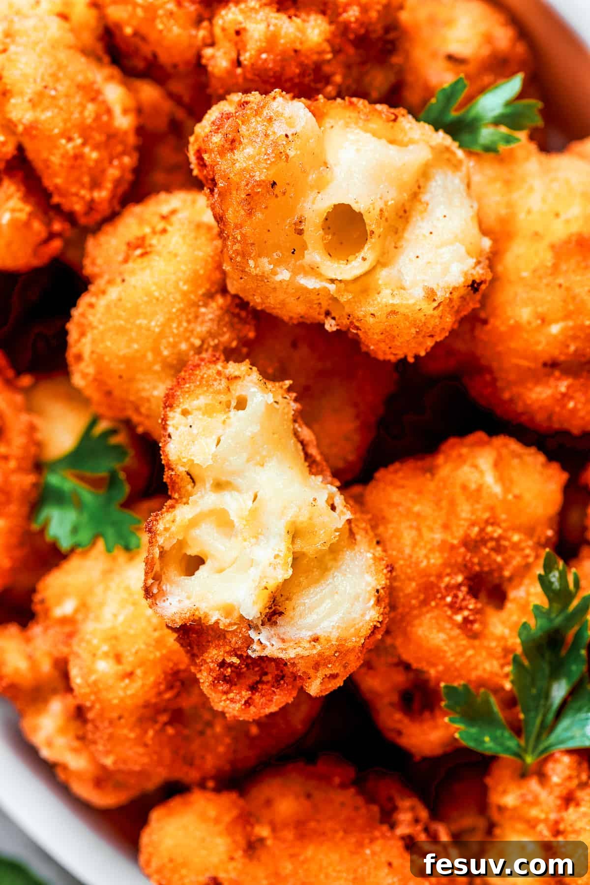 A close-up photograph of a fried mac and cheese bite, expertly cut in half to prominently display its incredibly rich, creamy, and gooey cheese interior.