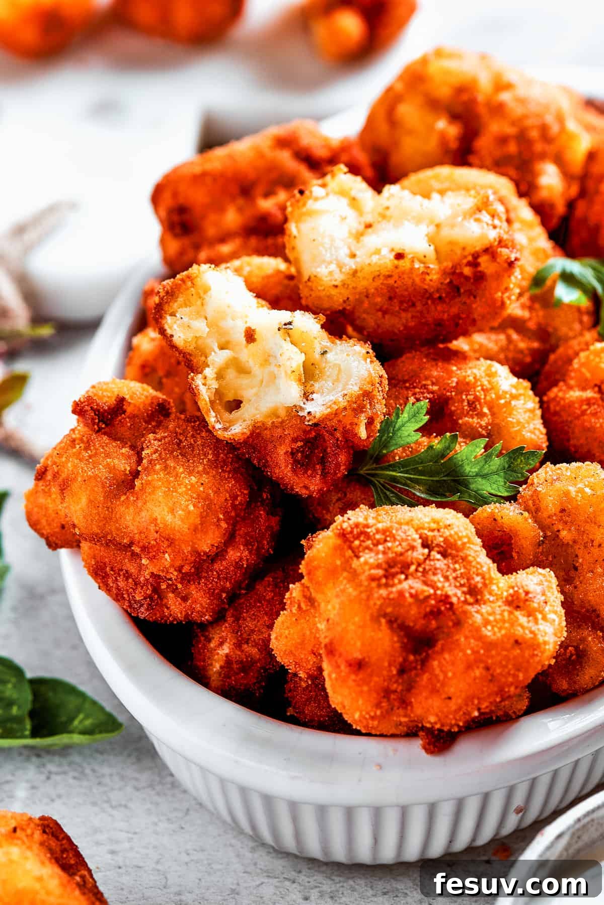 A large serving bowl generously filled with fried mac and cheese bites, beautifully arranged on a rustic wooden surface, with additional mac and cheese balls scattered around the bowl.