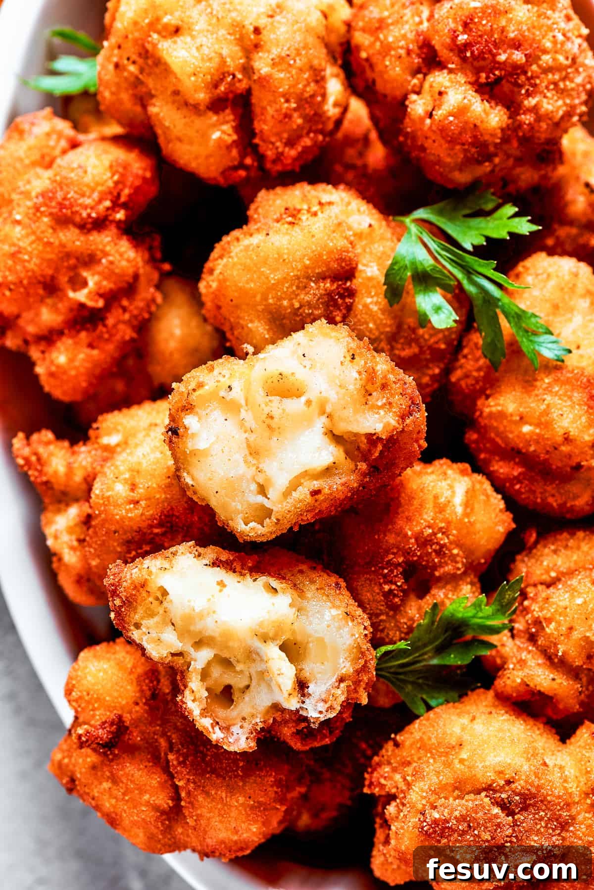 An overhead shot showcasing a beautiful serving bowl overflowing with golden-fried mac and cheese bites, elegantly garnished with fresh sprigs of herbs.