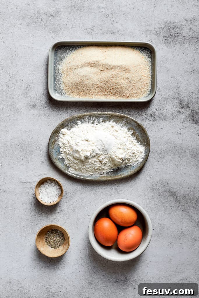 An overhead view of the organized breading station ingredients: a plate of all-purpose flour, a plate of crispy Panko breadcrumbs, a bowl of salt, a bowl of Italian seasoning, and a separate bowl with three whisked eggs.