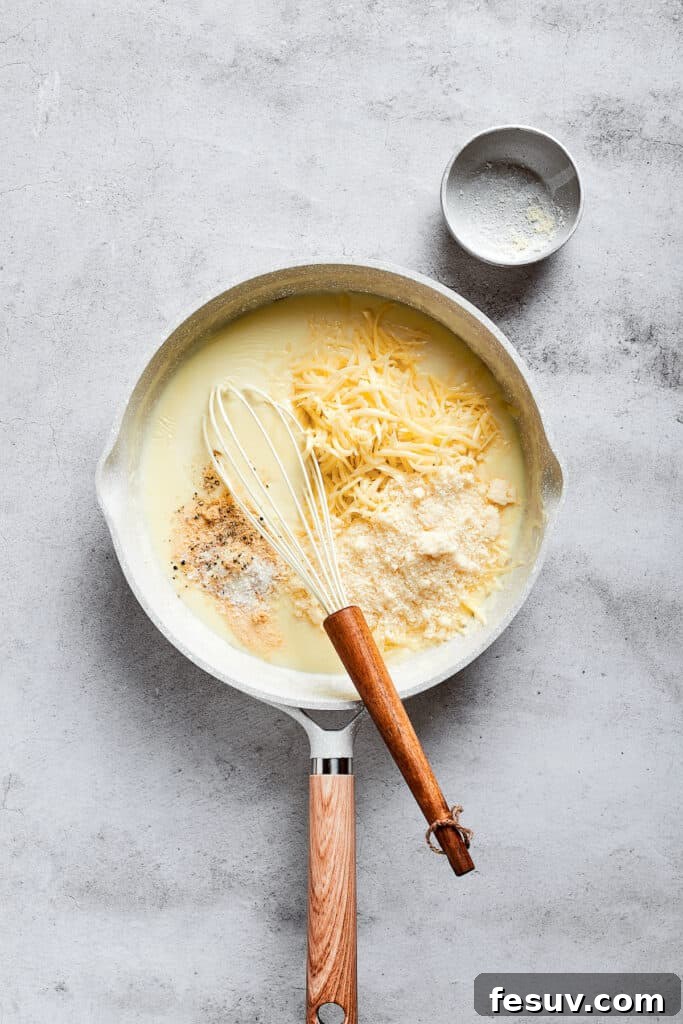 A saucepan on the stove, showing a whisk mixing shredded cheese into a creamy white milk mixture, forming a rich cheese sauce.
