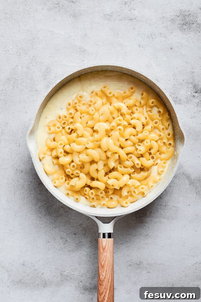 A saucepan filled with cooked elbow macaroni pasta resting on top of a generous amount of creamy, golden cheese sauce.