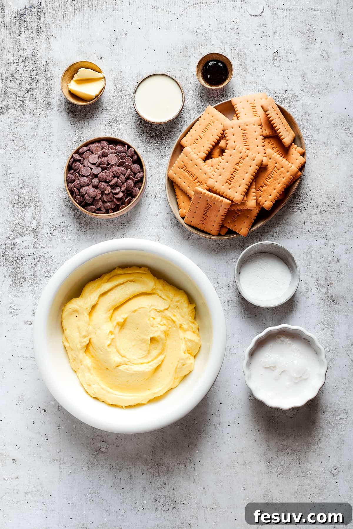 Overhead view of the ingredients needed for chocolate eclair cake: a bowl of vanilla pudding, a bowl of cookies, a bowl of chocolate chips, a bowl of cream, a bowl of milk, a bowl of butter, a bowl of vanilla, and a bowl of powdered sugar.