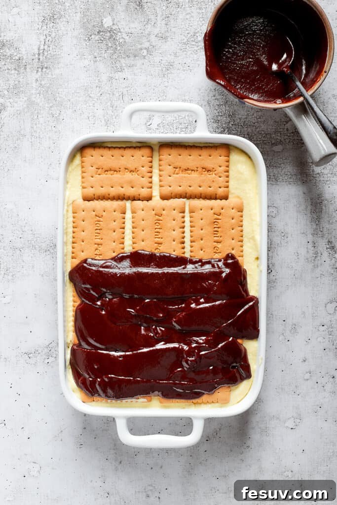 Overhead view of chocolate ganache half-spread over cookies in a baking dish.