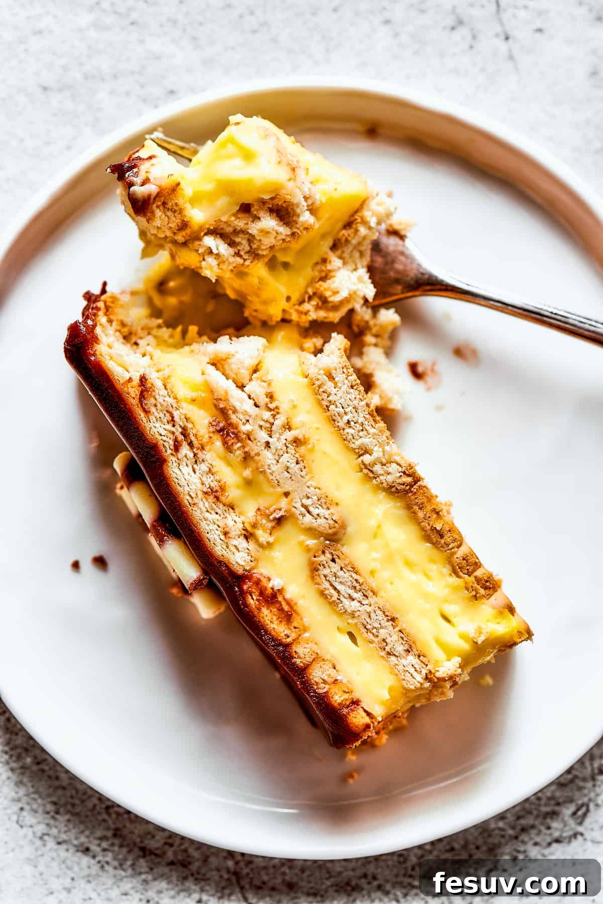 Overhead view of a piece of chocolate eclair cake on a plate, with a bit of it broken off with a fork.