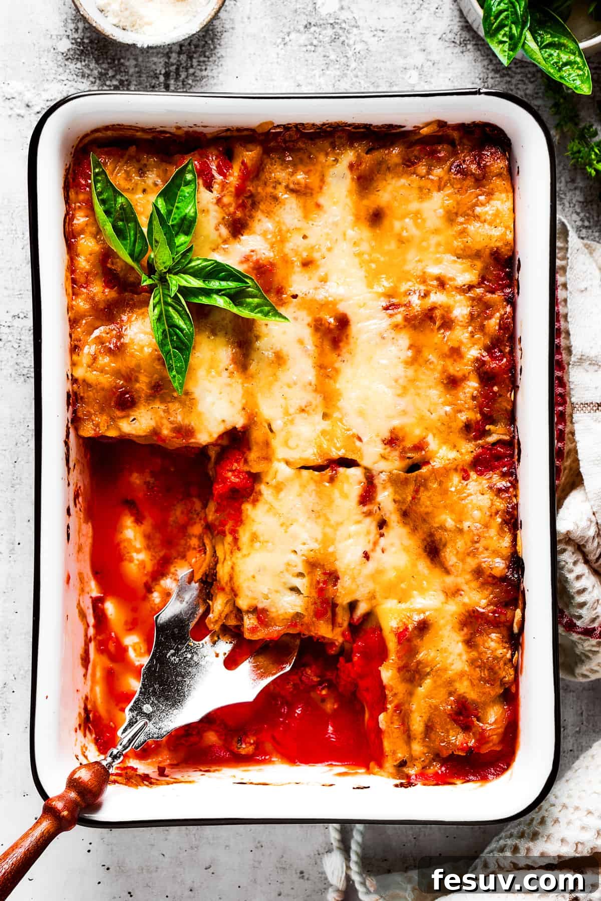 Easy lasagna roll ups have a beefy and herbaceous tomato sauce, a creamy cheese filling, tender pasta, and tons of melted cheese. Overhead view of a baking dish filled with lasagna roll ups with a few removed, and a serving spoon removing a roll.