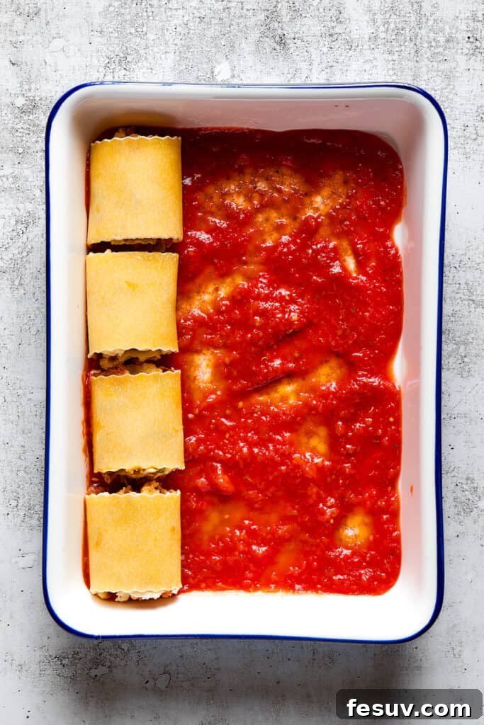 Baked Lasagna Pinwheels 3 Overhead view of a baking dish partially filled with unbaked lasagna roll ups on top of marinara sauce.