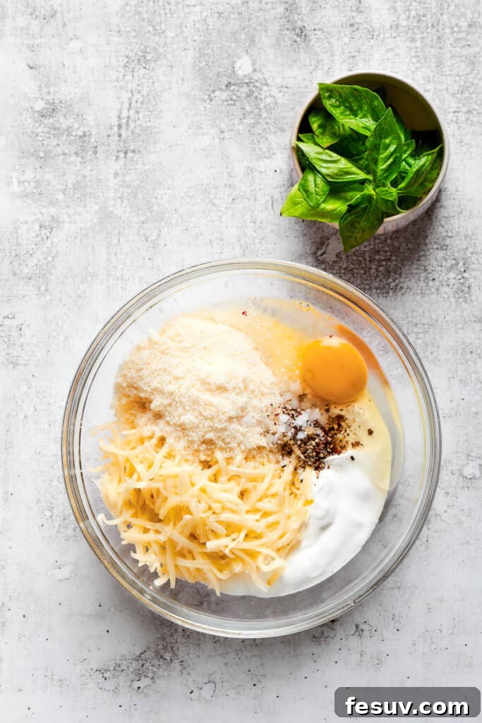 Easy lasagna roll ups have a beefy and herbaceous tomato sauce, a creamy cheese filling, tender pasta, and tons of melted cheese. Overhead view of a mixing bowl filled with parmesan cheese, mozzarella cheese, ricotta, an egg, salt, and pepper, next to a bowl of basil.
