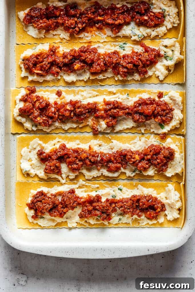 Easy lasagna roll ups have a beefy and herbaceous tomato sauce, a creamy cheese filling, tender pasta, and tons of melted cheese. Overhead view of lasagna noodles covered with a cheese mixture and a ragu.