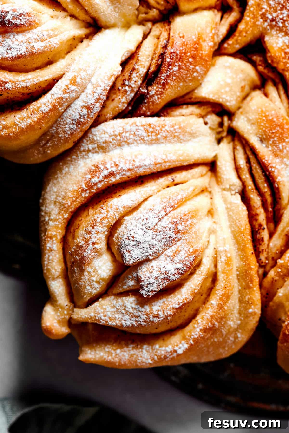 A close-up overhead shot of a single, perfectly golden and twisted segment of Star Bread, generously dusted with powdered sugar, highlighting its intricate layers and pull-apart texture.