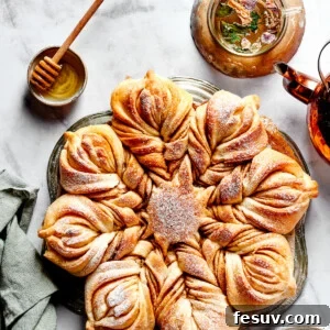 Overhead view of a star bread topped with powdered sugar, next to a bowl of honey.