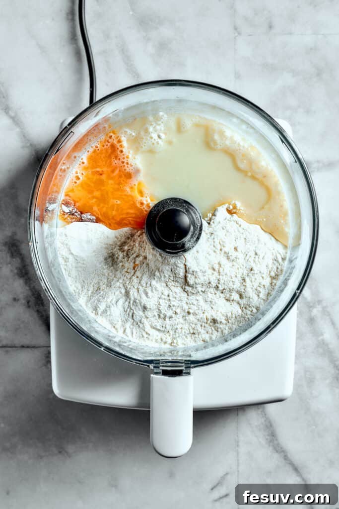 Overhead view of flour, egg yolk, milk, and yeast in a food processor, ready to be mixed into dough for Star Bread.