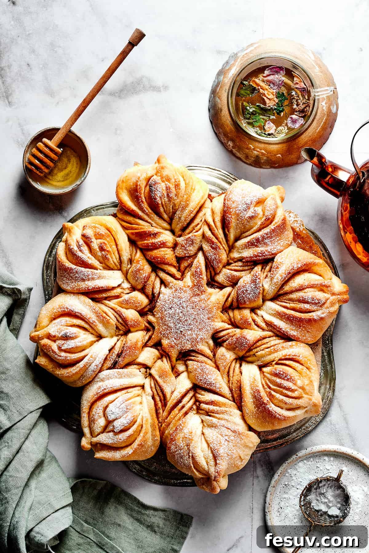 An inviting overhead view of a freshly baked Star Bread, artfully dusted with powdered sugar, resting on a wooden board next to a small bowl of honey. This holiday dessert is perfectly golden and ready to be enjoyed.