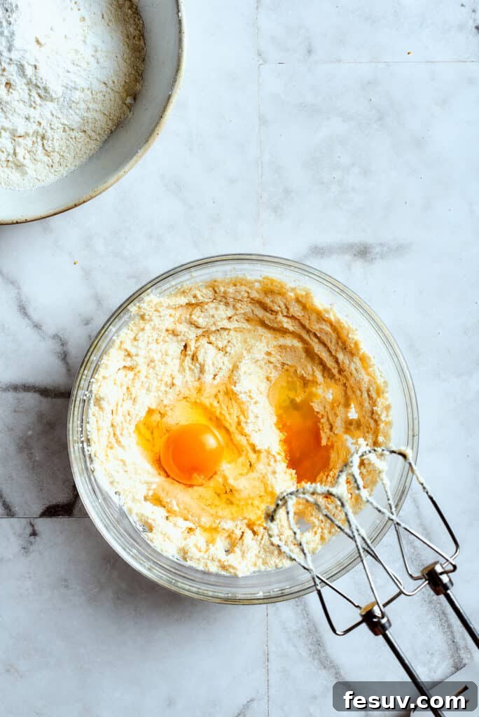 Overhead view of a mixing bowl with creamed butter and two eggs on top, with beaters.