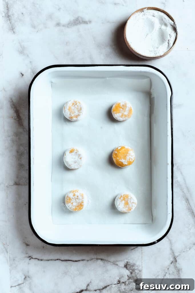 Overhead view of 6 balls of lemon cookie dough covered in powdered sugar in a baking tray.