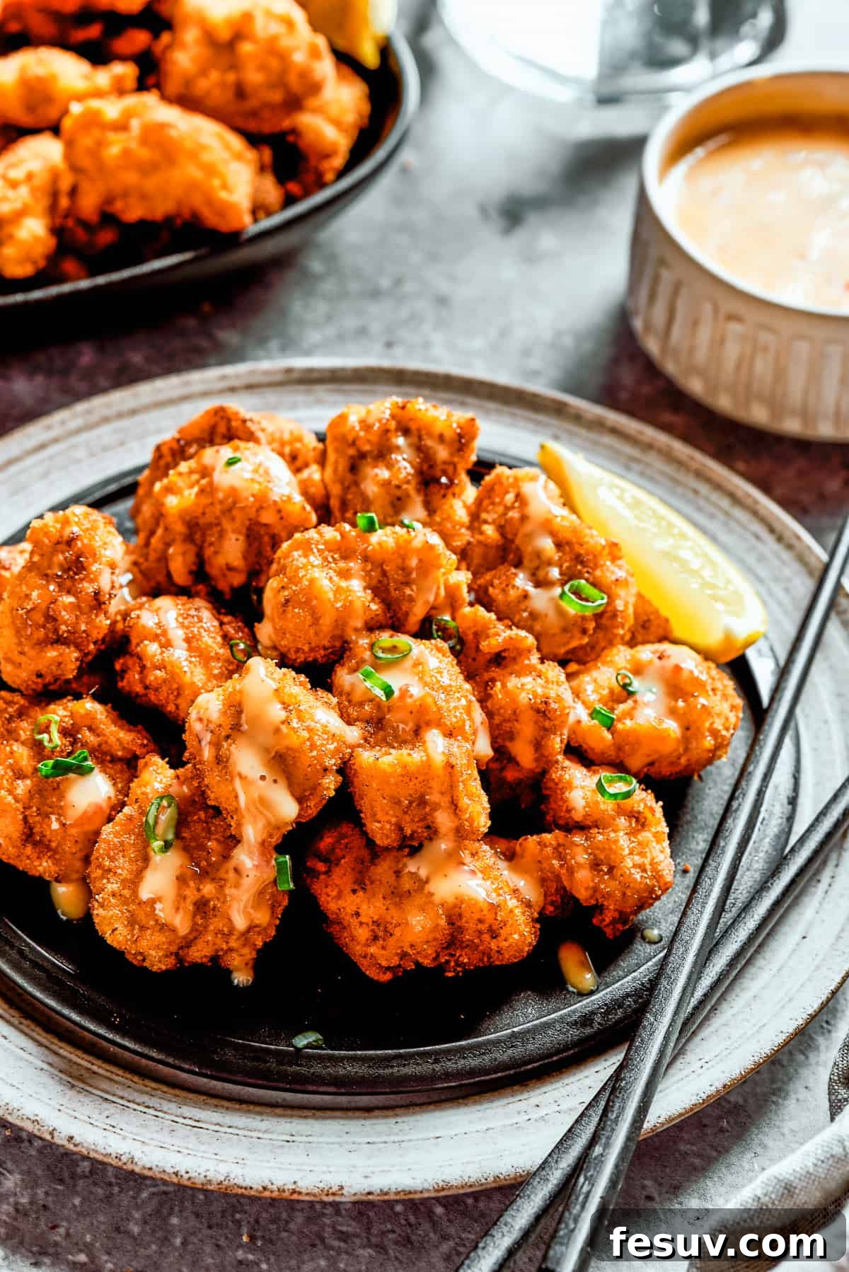 A plate of bang bang chicken with a lemon slice and a pair of chopsticks, next to a napkin and another lemon slice.