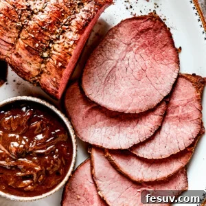 Top Round Roast Recipe Featured Image Image of a sliced beef roast served on a white platter with a bowl of gravy set next to it.