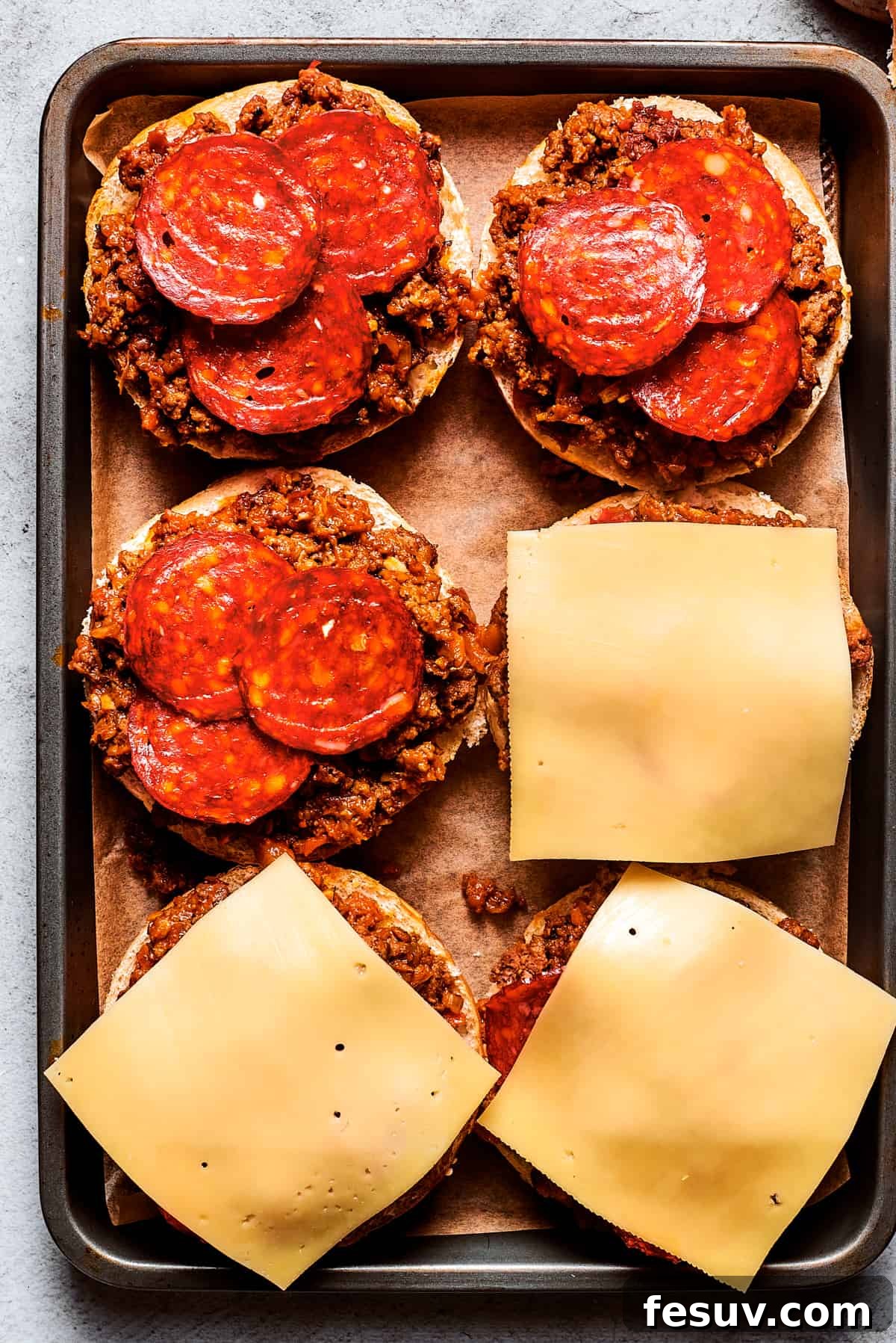 This easy Pizza Burger recipe is sure to become a family favorite! Meat filling is layered with pepperoni and melty mozzarella cheese. Cheese slices are placed on top of pizza burgers on a tray.