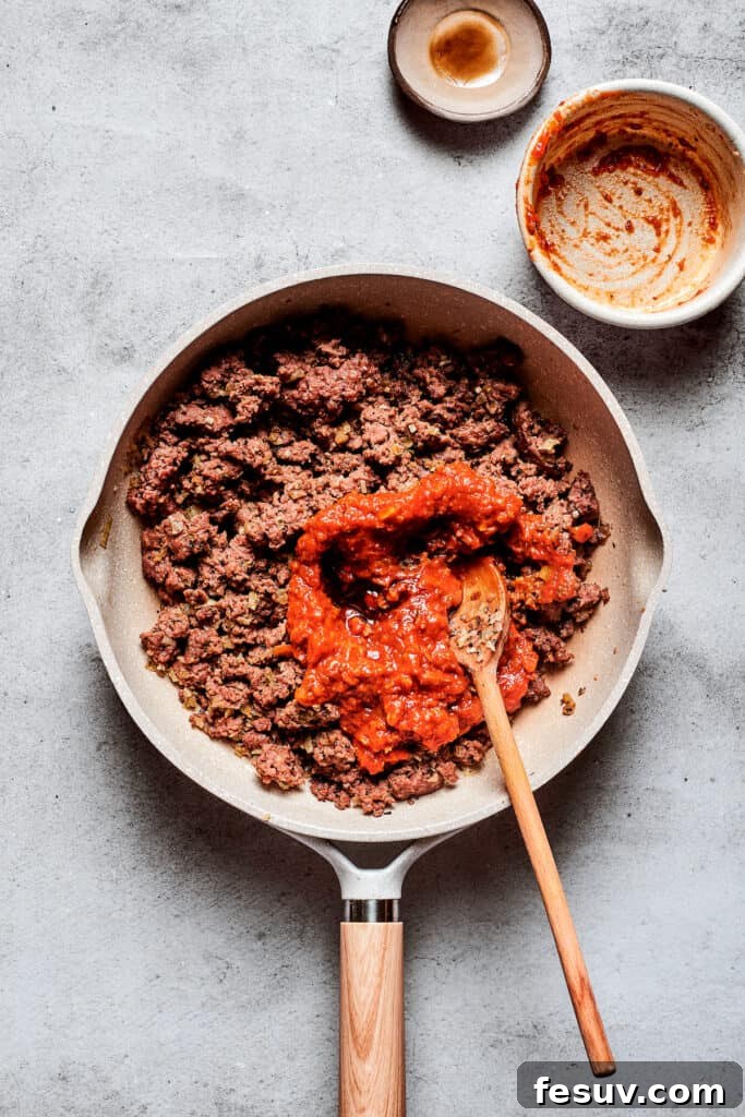 Pizzaburger 2 Pizza sauce is stirred into a pan of browned meat.