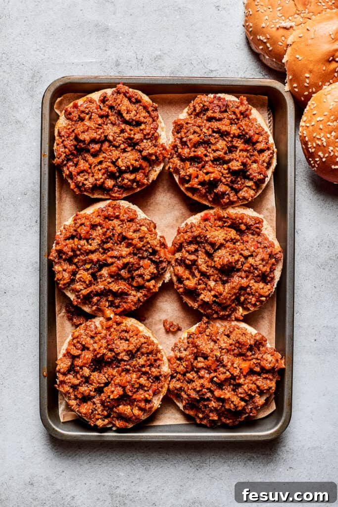 This easy Pizza Burger recipe is sure to become a family favorite! A hearty meat filling is layered with pepperoni and melty mozzarella cheese. Six pizza burgers with meat are shown on a baking sheet.