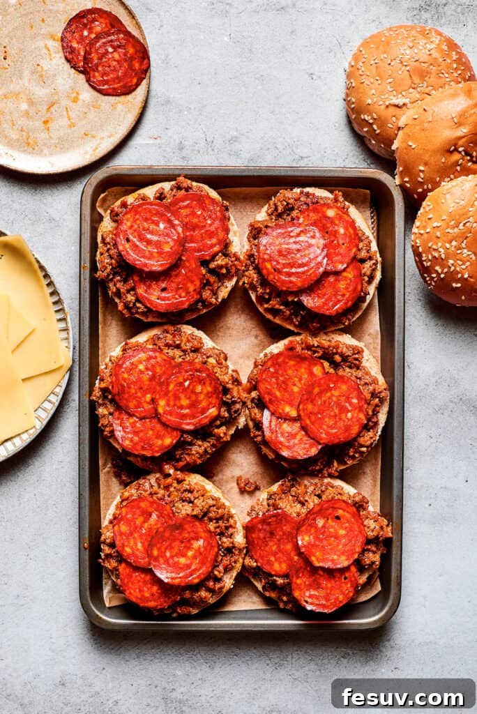This easy Pizza Burger recipe is sure to become a family favorite! Meat filling is layered with pepperoni and melty mozzarella cheese. Pepperoni is placed on top of pizza burgers on a tray.