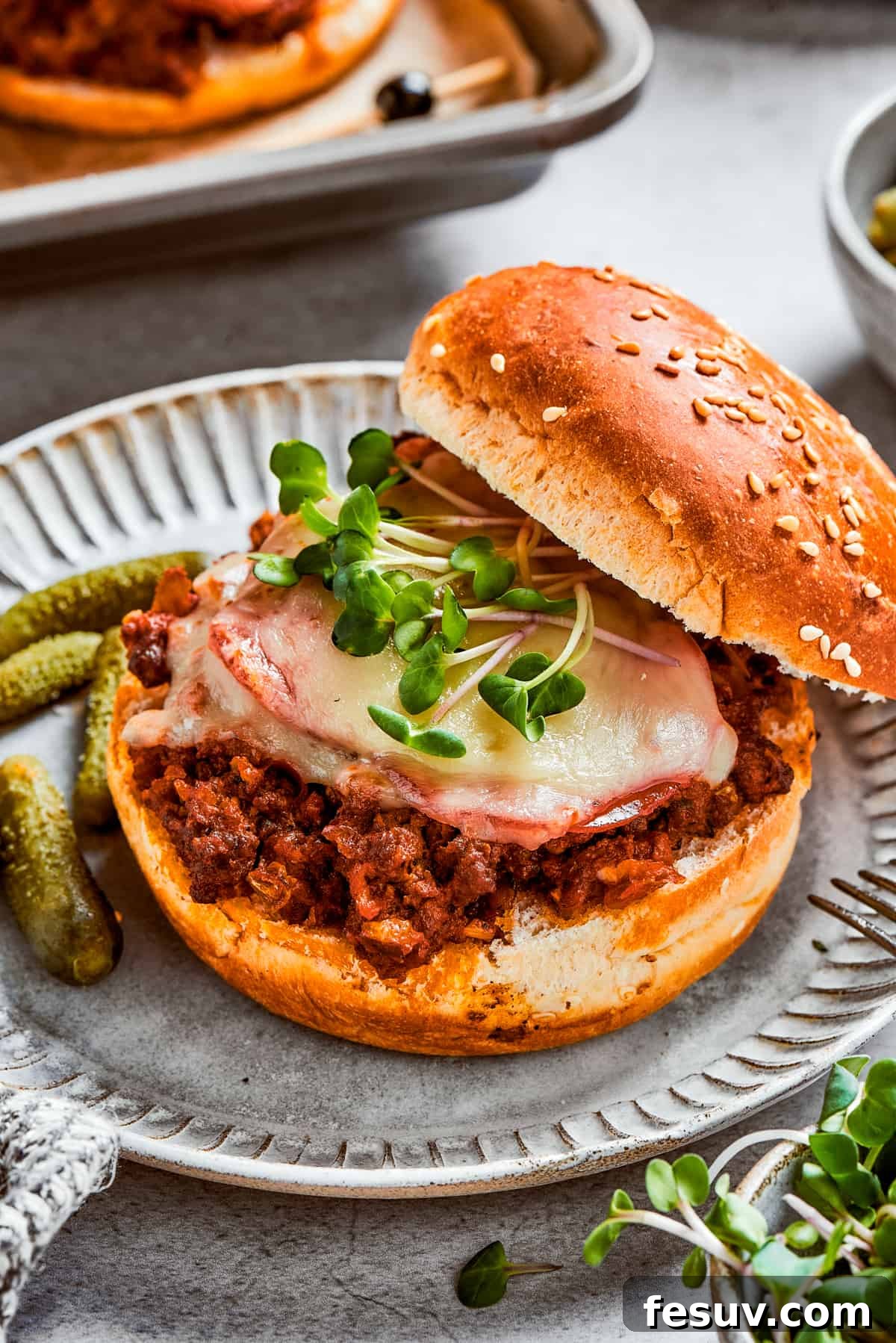 This easy Pizza Burger recipe is sure to become a family favorite! A hearty meat filling is layered with pepperoni and melty mozzarella cheese to make a wonderful toasted sandwich in just 30 minutes. Pizza burger with the top bun resting on the side of the burger so the filling is exposed.