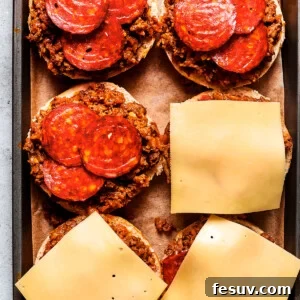 Cheese slices are placed on top of pizza burgers on a tray.