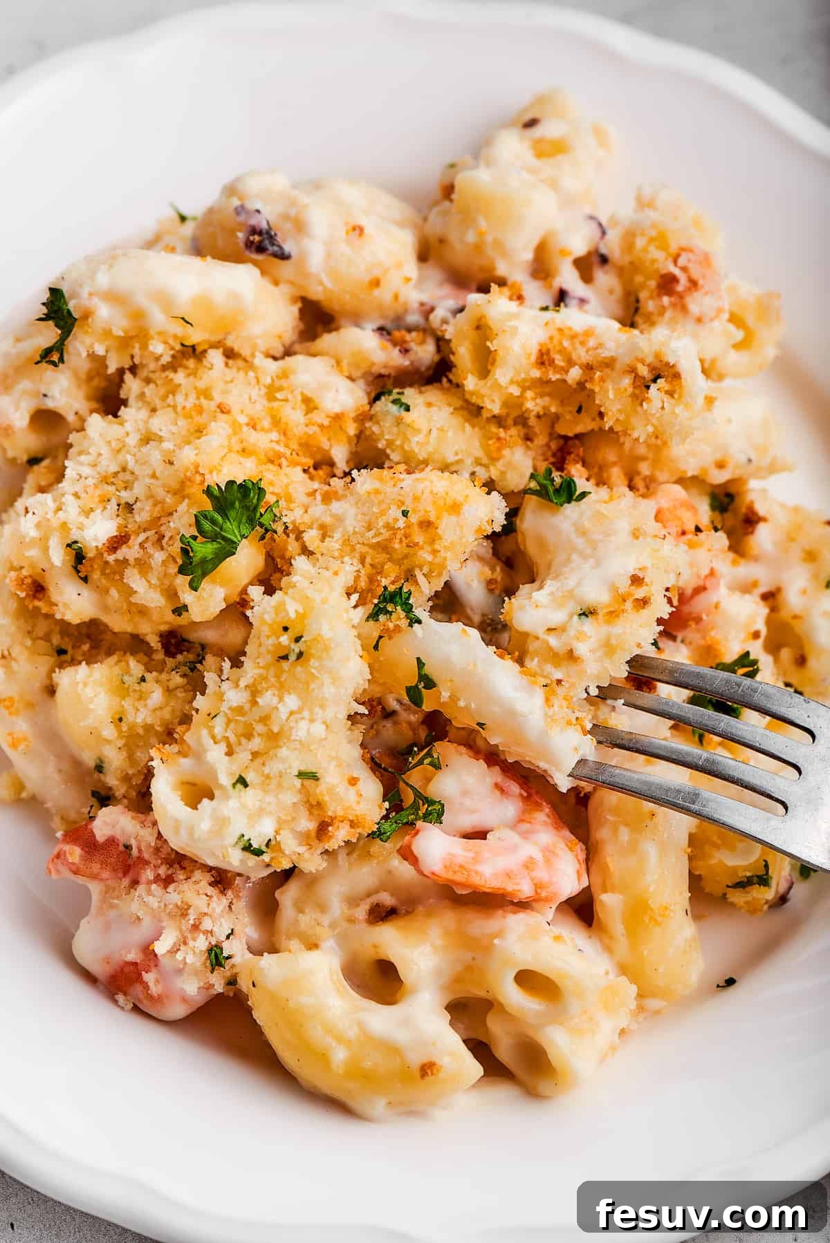 A person taking a bite of seafood mac and cheese from a fork, showing the creamy texture and generous seafood pieces.