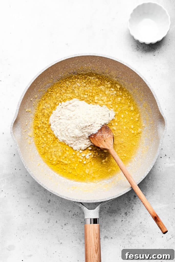 Adding flour to hot garlic butter in a saute pan to start the roux for the cheese sauce.