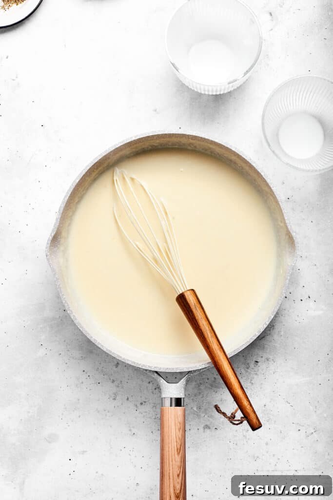 Pouring milk into the flour and butter mixture in a skillet to form the cheese sauce base.