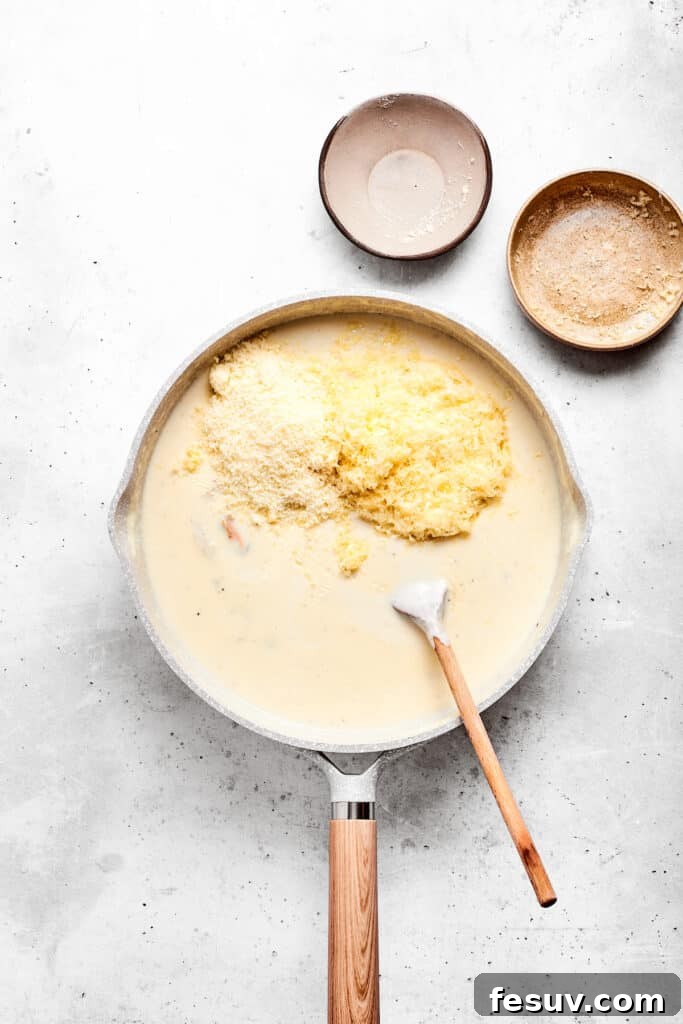 Stirring in grated cheese to the creamy sauce base, ensuring a smooth melt.