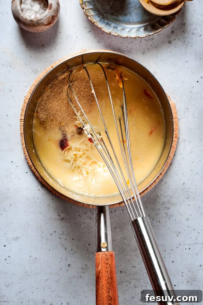 A whisk continuing to mix the rich, golden cheese sauce in a metal pot, illustrating the final stages of its preparation.
