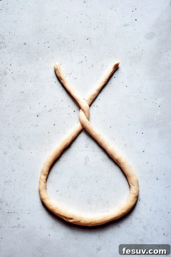 A long rope of soft pretzel dough being twisted into the classic pretzel shape, demonstrating the initial crossover.