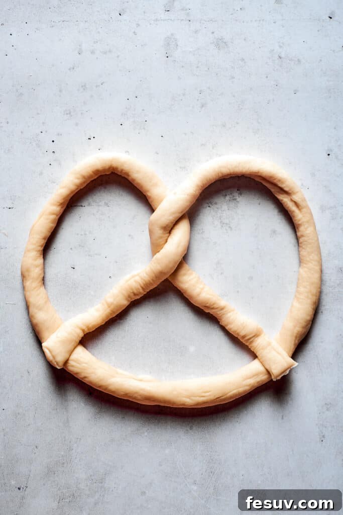 A rope of soft pretzel dough, now fully formed into the traditional pretzel shape, with its ends pressed into the bottom curve.