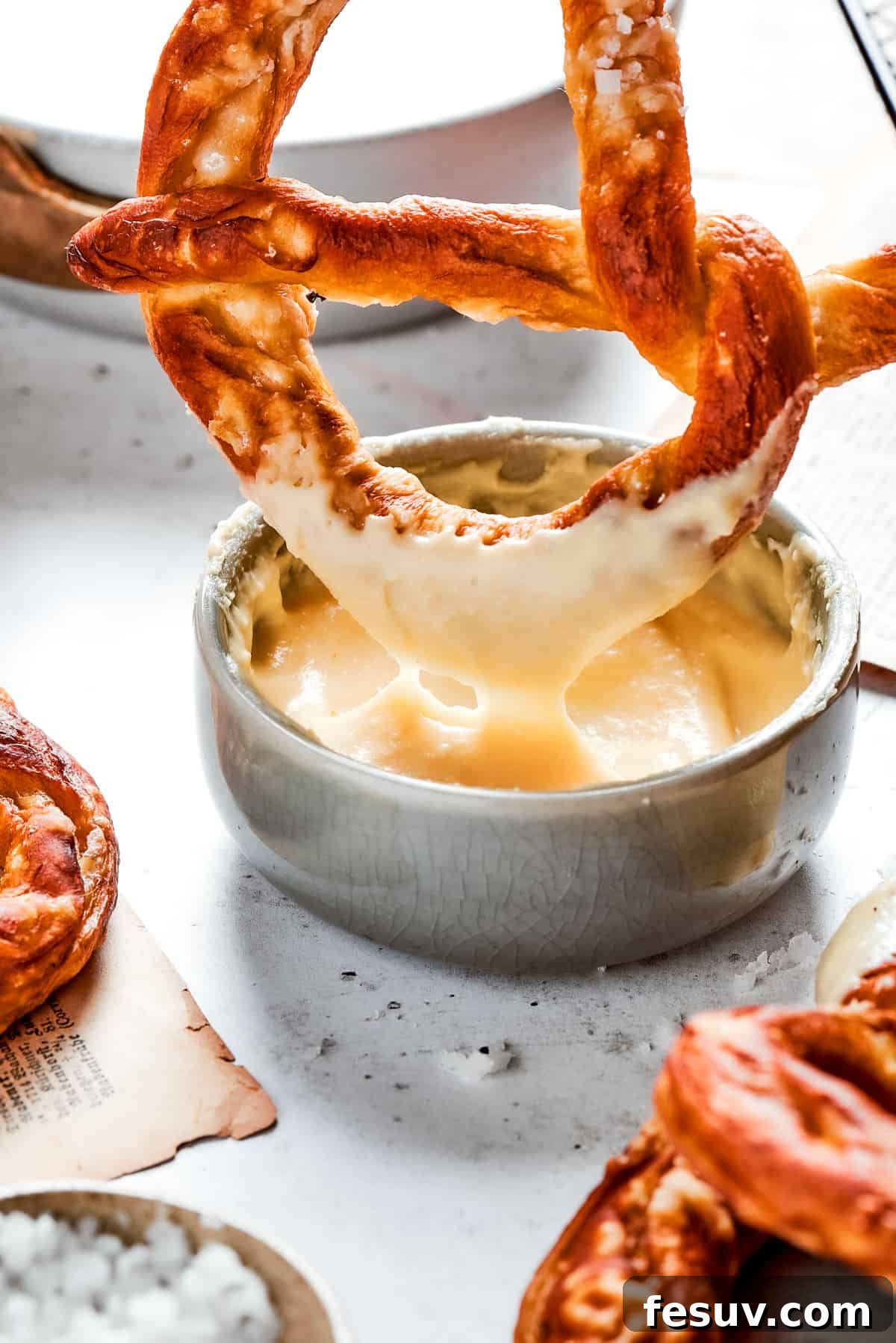 A perfectly baked soft pretzel being dipped into a rich, creamy cheese sauce, illustrating the ultimate way to enjoy this snack.