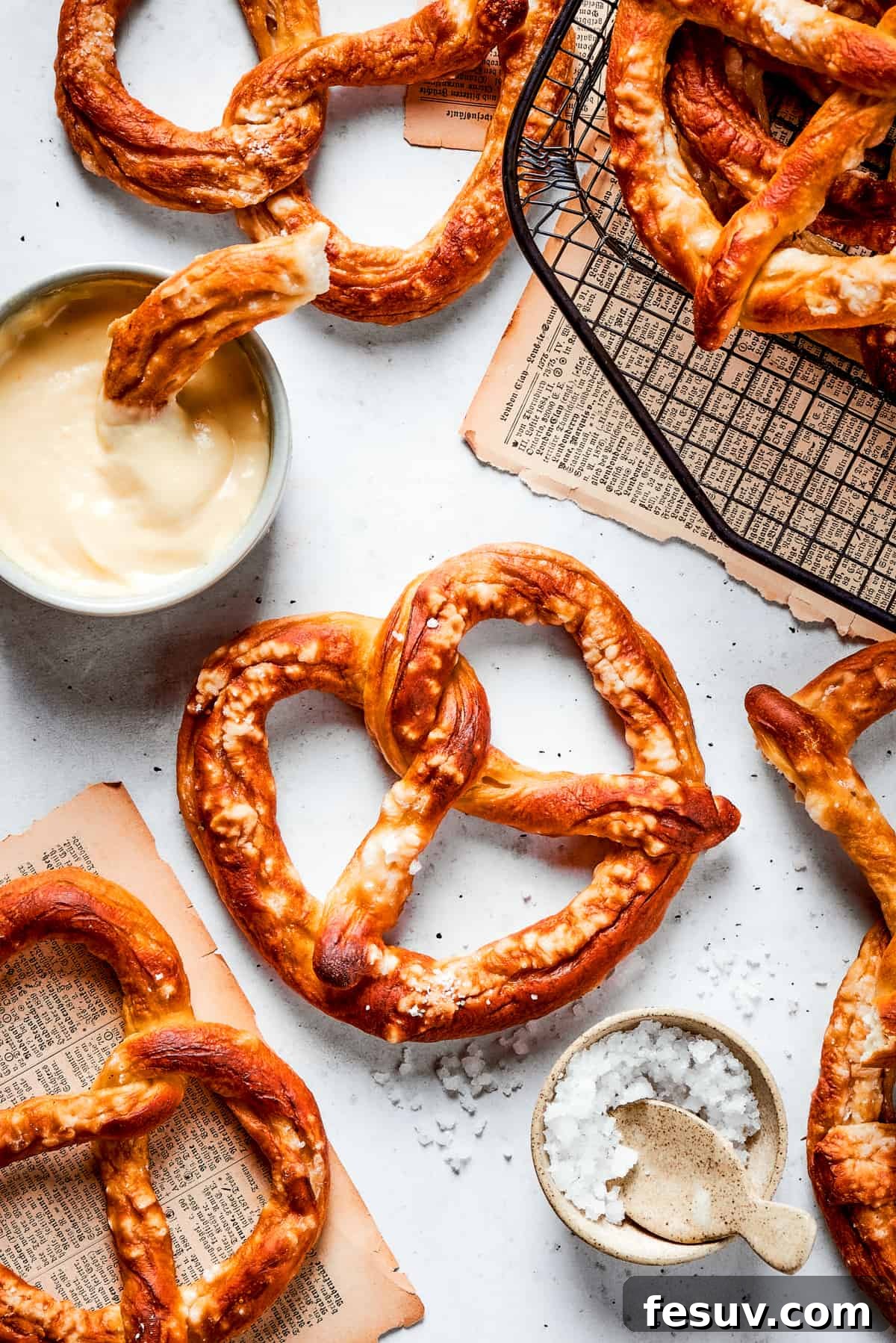 Baked soft pretzels are shown on a rack with cheese sauce alongside.
