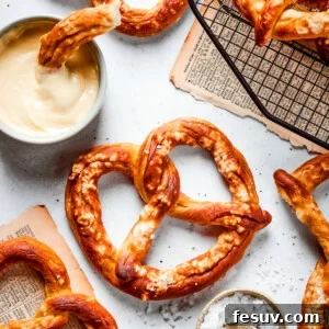 Baked soft pretzels are shown on a rack with cheese sauce alongside.