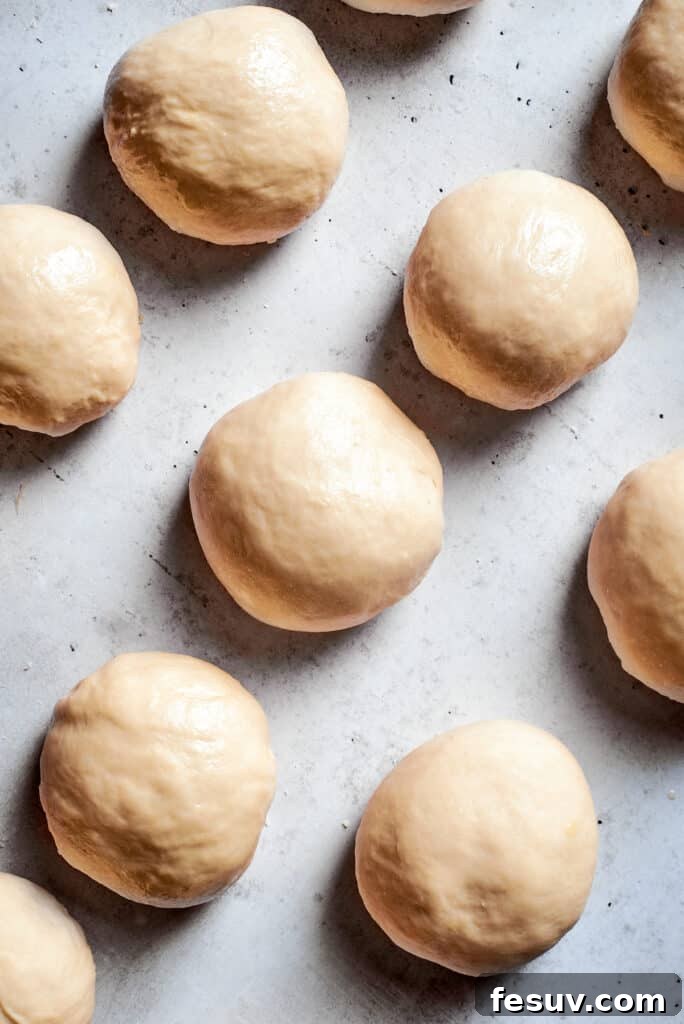 Small, uniform balls of soft pretzel dough on a clean white surface, prepped for rolling.