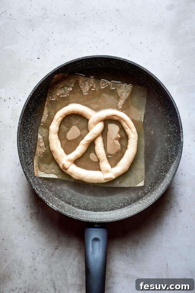 A soft pretzel submerged in a pot of boiling water and baking soda, undergoing its crucial bath.