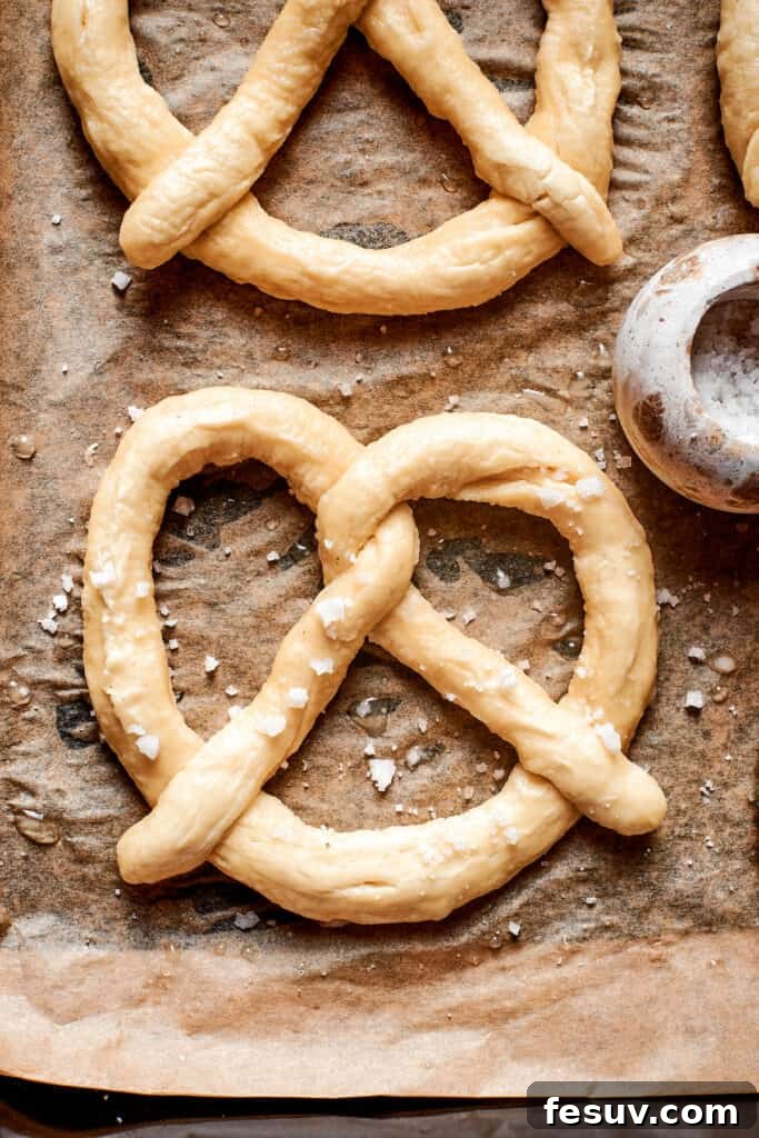 Several unbaked soft pretzels, freshly shaped and bathed, arranged on a baking sheet ready for the oven.