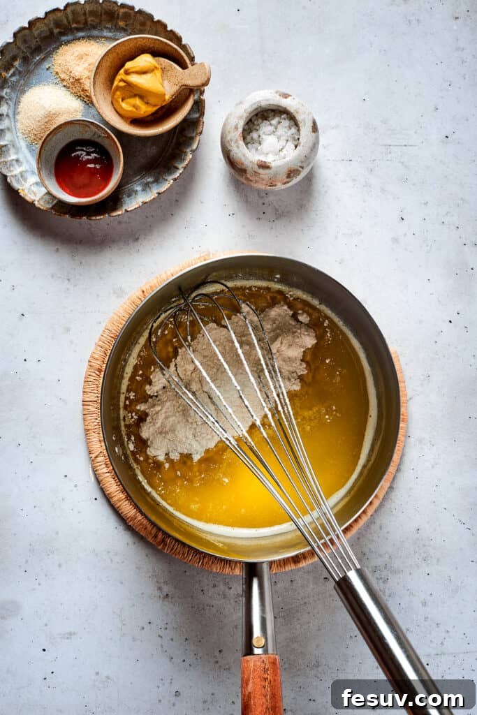 A whisk vigorously mixing a cheese sauce in a stainless steel pot, ensuring a smooth and creamy texture.